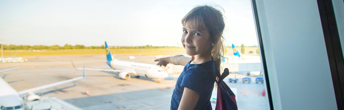 A child at an airport pointing at a plane through a window.
