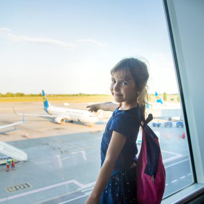 A child at an airport pointing at a plane through a window.