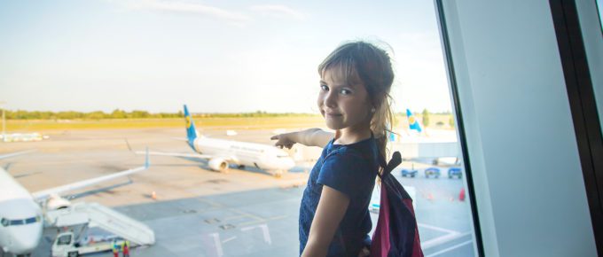 A child at an airport pointing at a plane through a window.