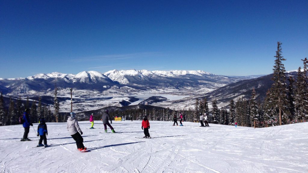 People skiing downhill in Colorado, the sky is blue and snowy mountains are in the distance.