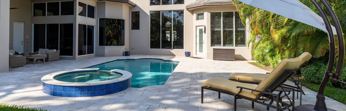 Backyard of a modern house with swimming pool, artificial grass, trees, chairs and an umbrella.