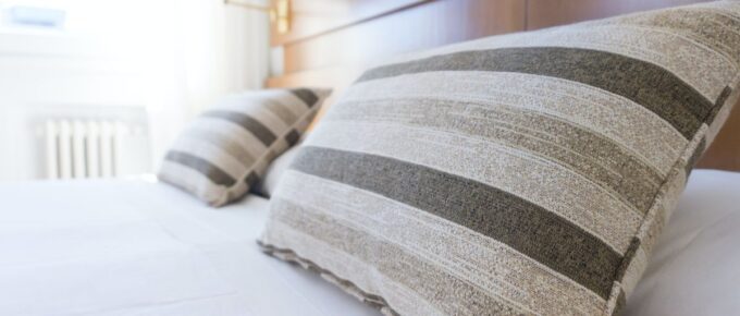 Gray and black pillow on white bed sheets in a hotel.