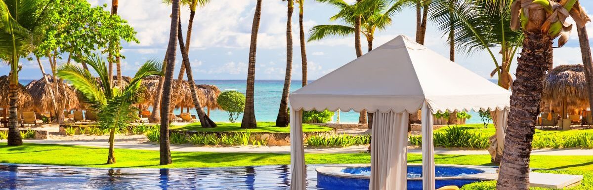 Caribbean beach resort with pool, palm trees, and white tent during the day.