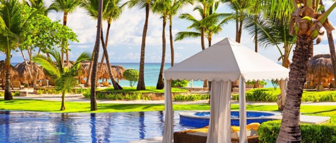 Caribbean beach resort with pool, palm trees, and white tent during the day.