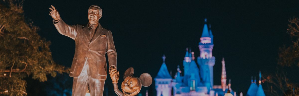 walt disney and mickey mouse statue with disneyland castle in the background at night