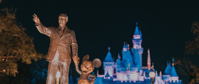 walt disney and mickey mouse statue with disneyland castle in the background at night