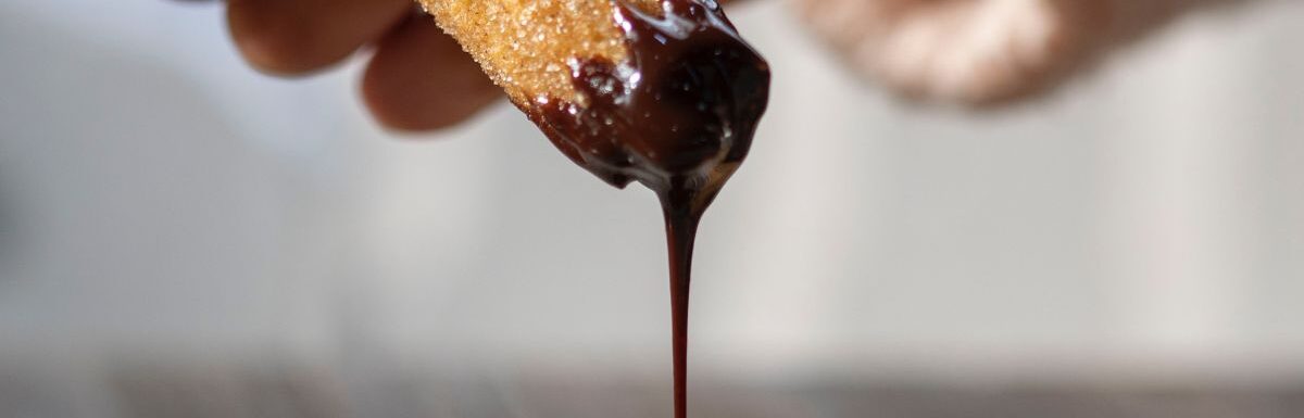 A woman holding churro while chocolate drips.