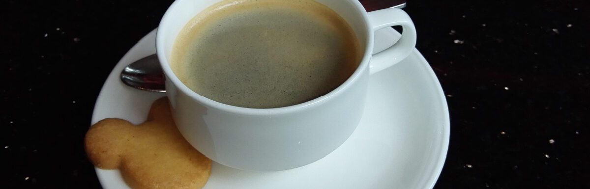 White cup with black coffee and Mickey Mouse shaped cookie.