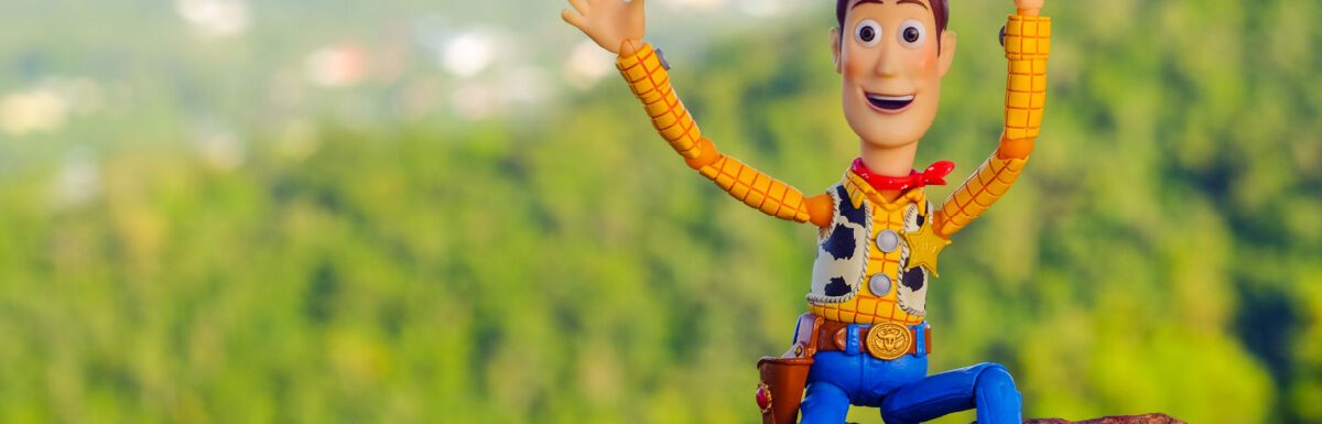 Woody of Toy Story movie sitting on the rock waving.