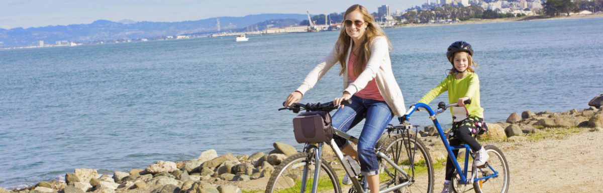 Mother and Daughter biking along the beach in California, USA.