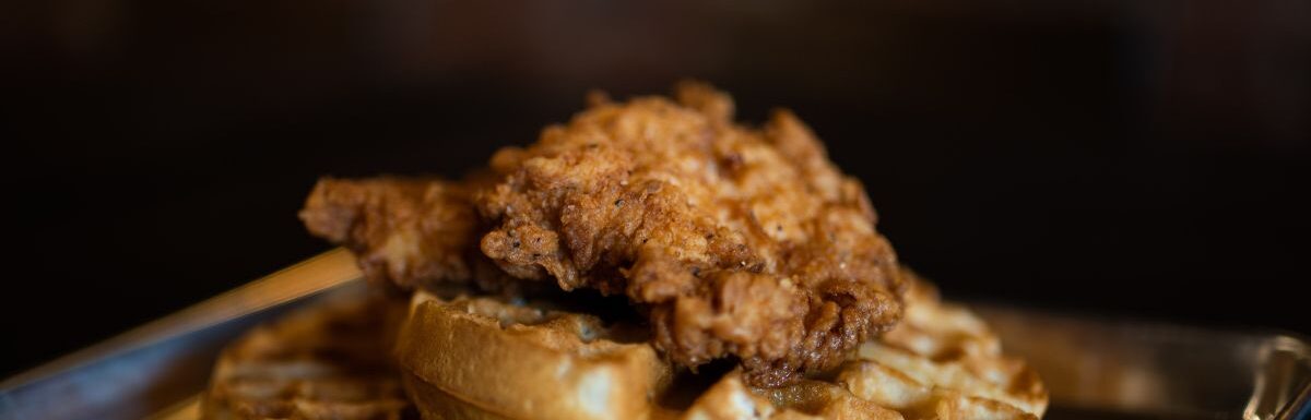 Waffle with fried chicken on top on a plate.