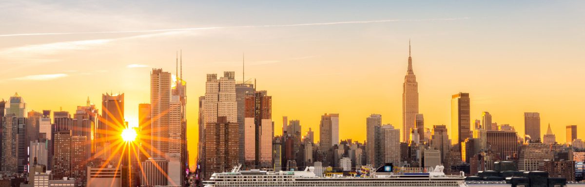 A large cruise ship sails Hudson river in New York while sun beams burst between the skyscrapers.