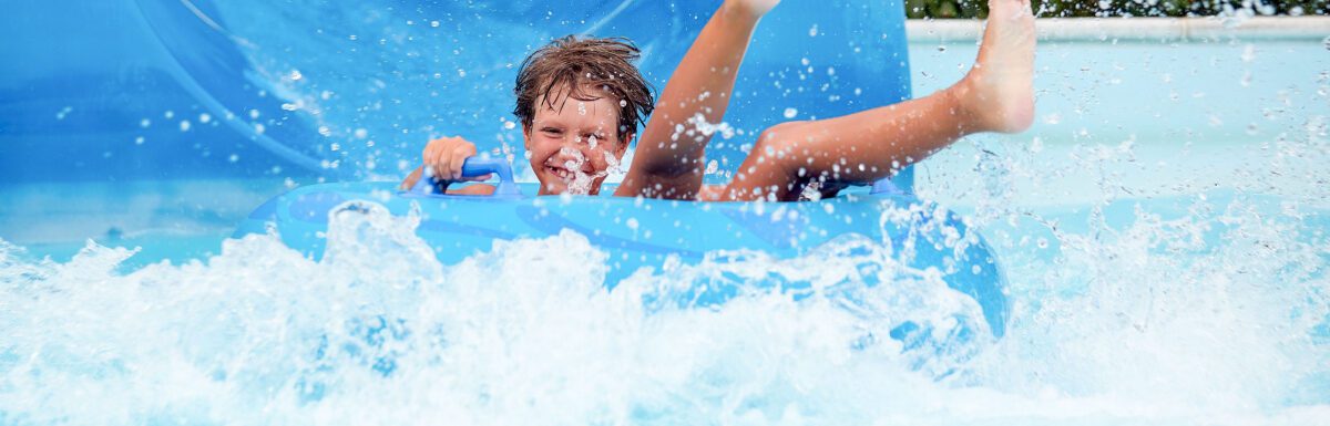 An 8 year old boy is riding in the water Park on inflatable circles on water slides with splash.