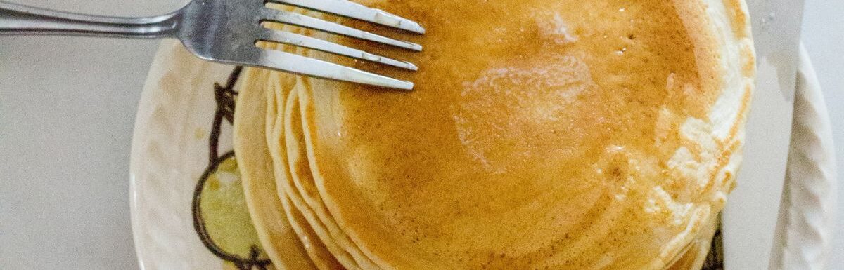 Pile of pancakes on a white plate with knife and fork.