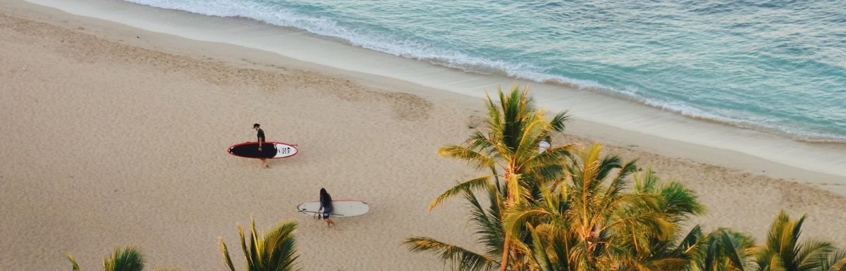 Two people carrying surf boards while walking in Queen's Beach, Honolulu, USA.