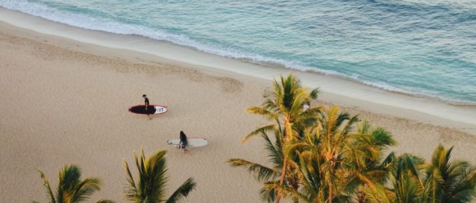 Two people carrying surf boards while walking in Queen's Beach, Honolulu, USA.