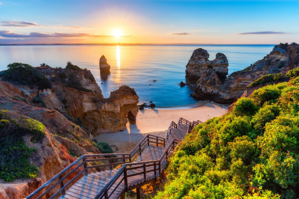 A beach in the Algarve taken from a cliff edge, showing the sun setting over the water