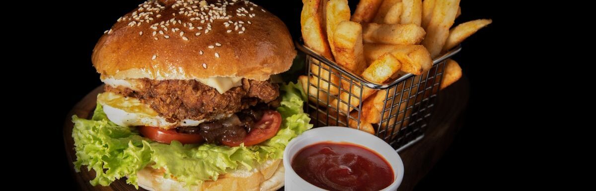 Hamburger, fries, and ketchup on a wooden platter and black background.