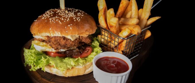 Hamburger, fries, and ketchup on a wooden platter and black background.