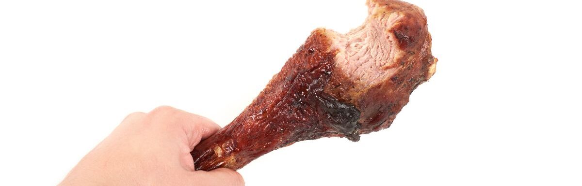 Hand holding roasted chicken leg with bite taken, isolated on white background.