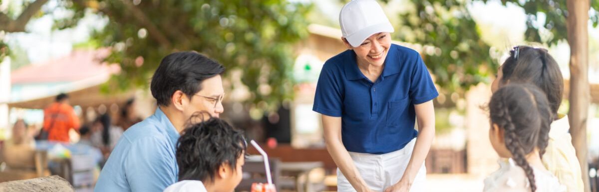 Waitress serving food and drink to customers on the table at beach restaurant at tropical island beach in sunny day.