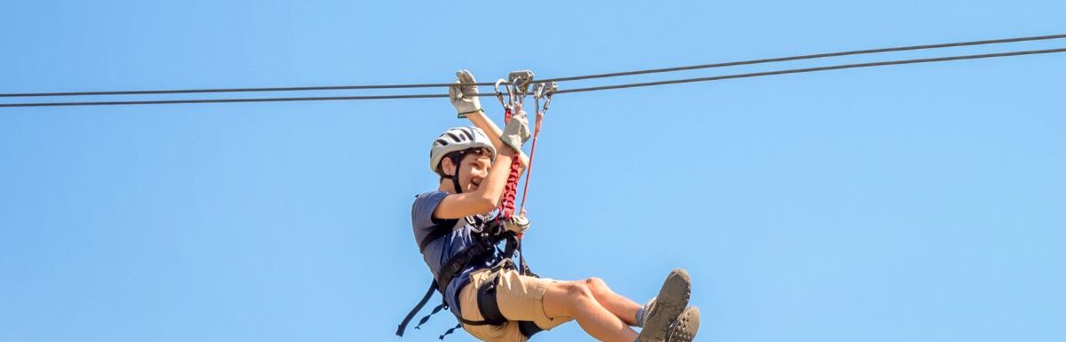 A teenager having fun on a zipline on panoramic blue sky background.