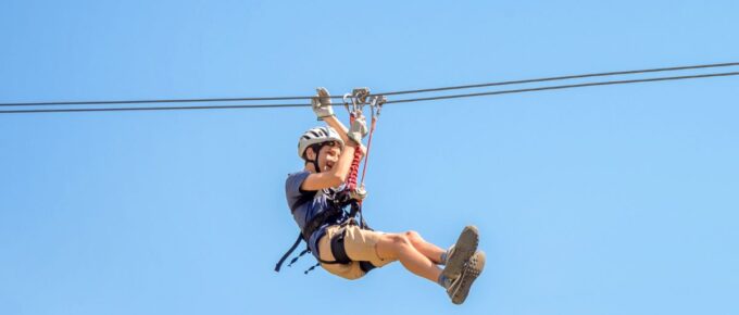 A teenager having fun on a zipline on panoramic blue sky background.