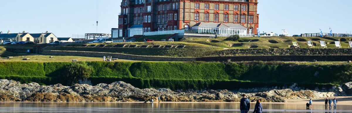 People and a dog in Fistral Beach and The Headland Hotel and Spa in Newquay, Cornwall, England.