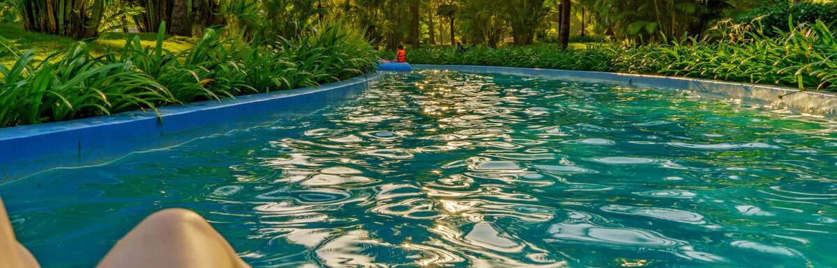 A person floating on a lazy river in a resort with palm trees around on an afternoon.