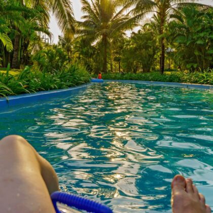 A person floating on a lazy river in a resort with palm trees around on an afternoon.