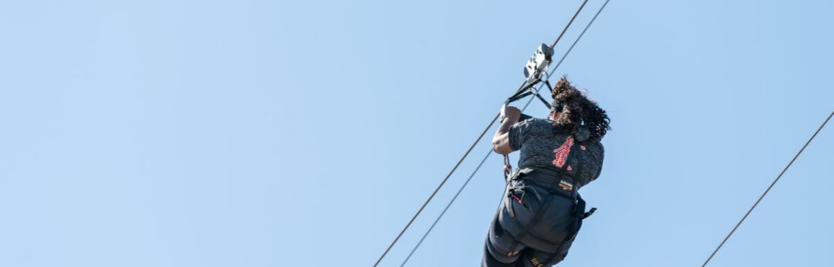 Back of one young American woman isolated against a blue sky on a zipline.
