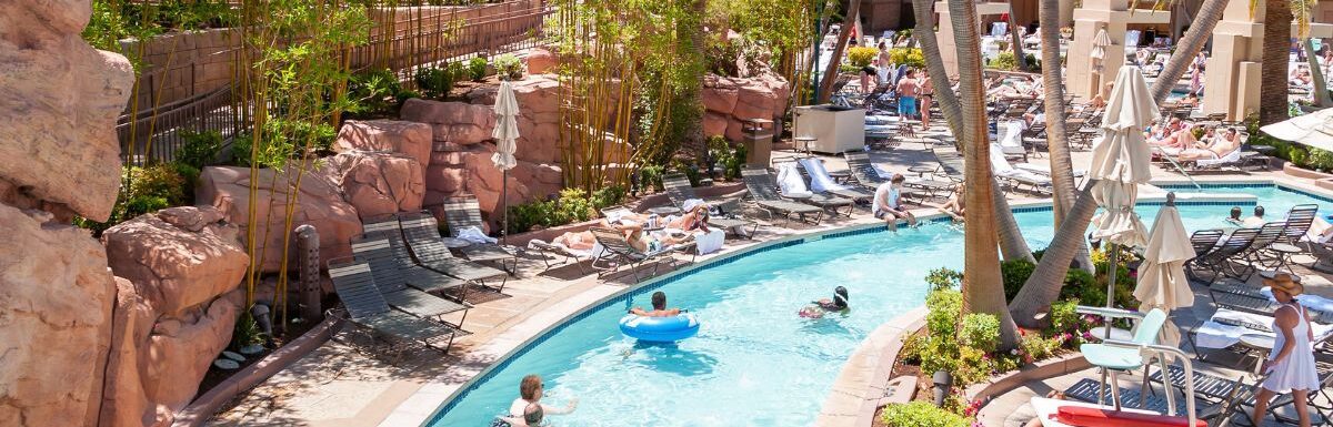 Lazy river pool in a hotel with people and trees around during the day.