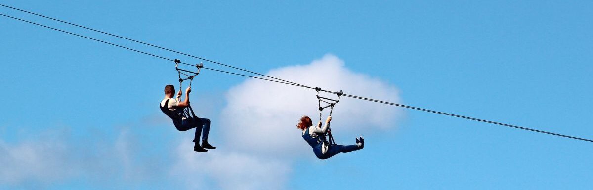 Man and woman descend on a zipline during day time.